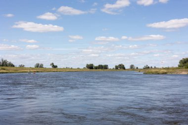 Elbe Nehri 'ni geç, Saksonya-Anhalt' da. Nehrin solunda ayakta duran bir kürekçi. Mavi gökyüzü, kıyı yeşil çalılar ve ağaçlarla.