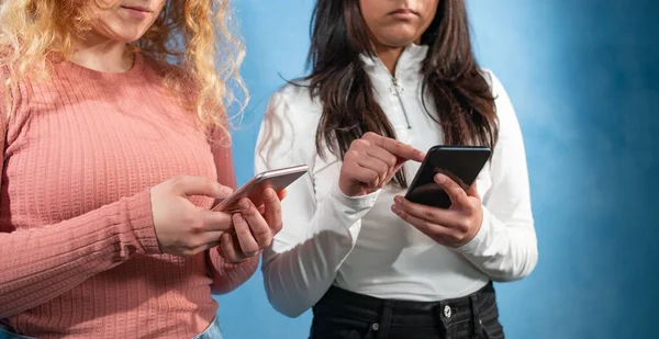 两个年轻人在手机上打字 两个年轻女子站在蓝色的背景上 他们在思考 在手机上打字 — 图库照片
