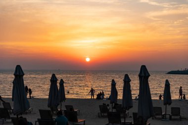 Birleşik Arap Emirlikleri, Dubai, Nisan 2023, La Mer Sahili, akşam. Dükkanları, restoranları, kafeleri ve plajı olan güzel bir yer. Şemsiye silueti ve sahildeki insanlar..