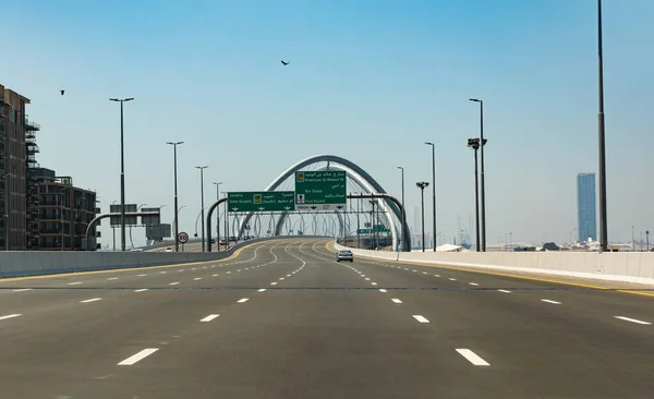 stock image Dubai, United Arab Emirates - April 21th 2023: Empty Infinity Bridge road with only one car. Direction Port Rashid and Dubai down town. Blue sky with birds. Infinity Bridge behind the road sign. 