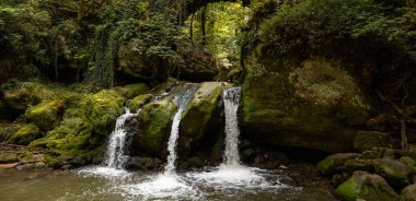 Mullerthal, Lüksemburg tepelerinde Schiessentempel şelalesi. Kara Ernz nehri vadiden akar. Yaz, yeşil yosun, orman.