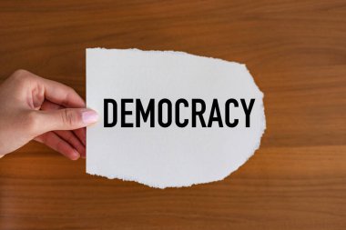 Demokrasi. Kadın eli, üzerinde bir not olan bir kağıt parçası tutuyor: Demokrasi. Cumhuriyet, egemenlik, özerklik, siyaset, insan hakları, siyaset.