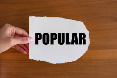 Popüler. Kadın eli, üzerinde bir not olan bir kağıt parçası tutuyor. Popüler. Ünlü, kabul edilmiş, sevilen, çekici, modaya uygun, tanınmış.