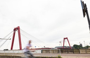 Rotterdam 'daki Willems Köprüsü, Nieuwe Maas' ı kapsıyor. Ön planda bulanık biri var. Öğleden sonra bulutlu bir gün.