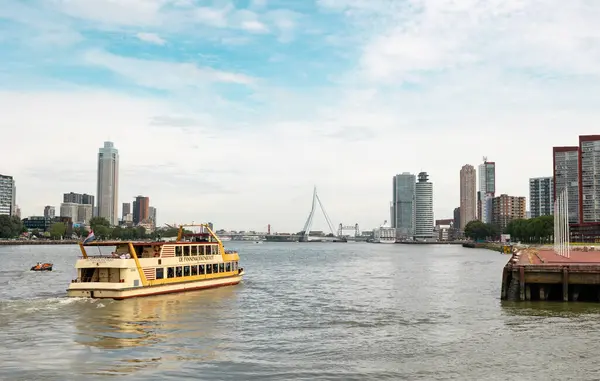 stock image Rotterdam Netherlands - July 9, 2024: View of the city with the Erasmus Bridge and the cruise terminal. In the foreground an excursion boat with tourists.