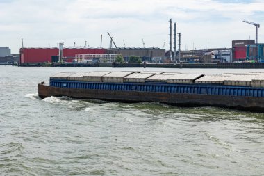 Rotterdam, Hollanda - 9 Temmuz 2004: Endüstriyel malların nakliyesi için bir gemi Rotterdam kargo limanından geçer. Arka planda depolar, sanayi tesisleri ve endüstriyel vinçler var..