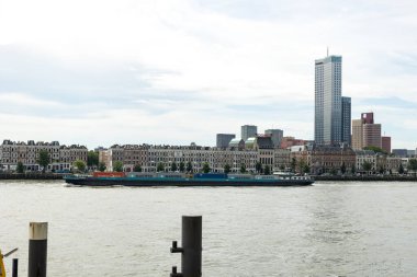 Rotterdam, Hollanda - 9 Temmuz 2004: Ofis ve konut binalarının manzarası ve Noordereiland 'daki Maaskade' nin tarihi perdesi. Konteynırlı büyük bir nakliye gemisi geçiyor..