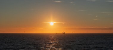 Kuzey Denizi 'nin üzerinde gün batımında bir gemi silueti ve ufukta bir rüzgar çiftliği olan Panorama..