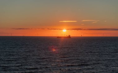 Güneşe yakın bir nakliye gemisinin silueti. Arka planda rüzgar tarlası, günbatımında Kuzey Denizi, Hollanda.
