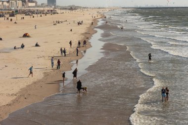 Lahey, Hollanda - 10 Temmuz 2024: İnsanlar gün batımında Scheveningen 'de halk plajında realaxing ve yürüyüş yapıyorlar. Arka planda sörf yapan uçurtma sörfçüsü.