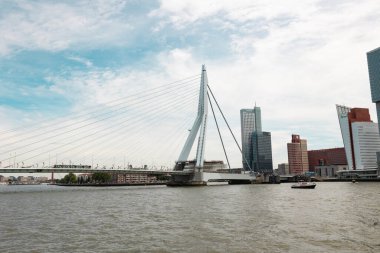 Rotterdam Hollanda - 9 Temmuz 2024: Erasmus Köprüsü 'nün bir kısmı, nehir tarafından görüş. Köprüde bir tramvay çalışıyor. Gökyüzü bulutlarla dolu..