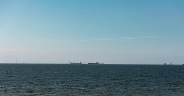 Hollanda 'daki Kuzey Denizi' nde nakliye gemileri, arka planda açık deniz rüzgâr çiftliği. Mavi gökyüzü, sakin deniz, yaz.