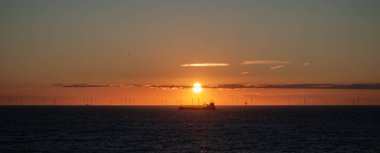 Nakliye gemisi ve açık deniz rüzgâr çiftliği Kuzey Denizi ufkunda gün batımında. Az bulut, altın gökyüzü. Hollanda, Scheveningen, Lahey.