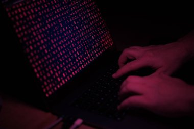 Eller bilgisayarın klavyesinde daktilo, kırmızı ışık, siber suç. Teknpoloji, siber saat, sistem hacklenmesi, virüs, ikili kod.