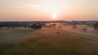 Foggy Kentucky Çiftliği üzerinde 4K Hava / Drone Fly uçuşu. Sabah Gündoğumu Görünür. Arka planda sisli göl görünüyor. Çiftlik evi, dört tahtalı çit, görülebilir tarlalar..