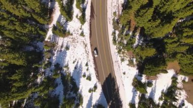 4K Hava İHA 'sı, karlı çam ormanlarında park halindeki aracın üstünde yükseliyor. Uzun gölgeler. Araba geçiyor..