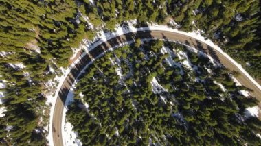 4K Aerial Drone Top Down Karlı çam ormanında yol kıvrımında yükseliyor. Uzun gölgeler. Araba geçiyor..