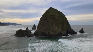 4K Hava Aracı, Oregon saman yığını kayasının yörüngesinde dönüyor. Dalgalar ve kıyı şeridi görünür..
