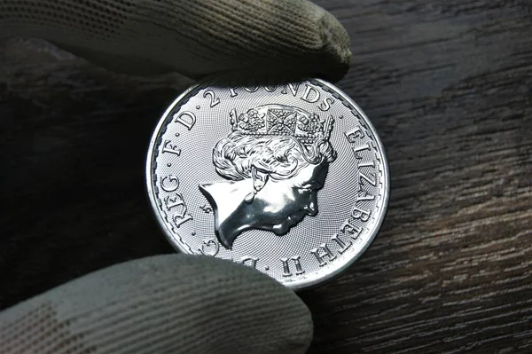 A British silver investment coin in the hands of a numismatist. British silver coin 2 Pounds proof.
