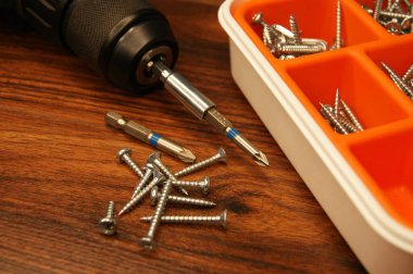 Koyu ahşap bir yüzeyde bir kutu vida ve bir vida tabancası.