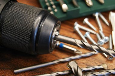 Ahşap arka planda matkaplar ve çeşitli malzemelerle hazırlanmış bir matkabın yakın plan çekimi..