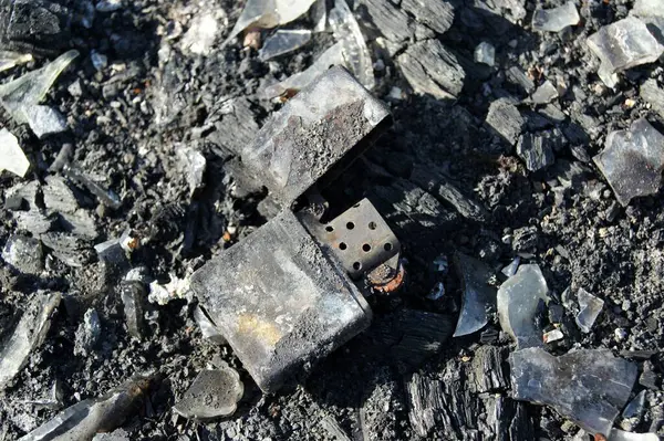 Yangının sonuçları. Kül içinde yanmış metal çakmak. Yakın plan..