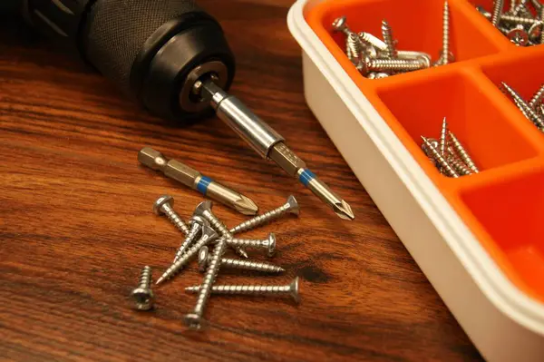 Koyu ahşap bir yüzeyde bir kutu vida ve bir vida tabancası.