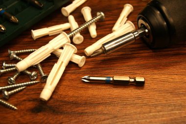 Koyu ahşap bir yüzeyde vidalar, plastik perdeler ve tornavida. Assembler 'in çalışma süreci.