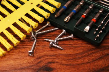 Vidalar, plastik kaplar ve tahta bir masanın üzerindeki parçalar.