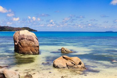Kayalık bir sahil şeridi, Anse Takamaka plajı yakınlarındaki Praslin Adası açıklarındaki mavi suları vurguluyor.