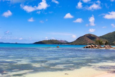 Kayalık bir sahil şeridi, Anse Takamaka plajı yakınlarındaki Praslin Adası açıklarındaki mavi suları vurguluyor.