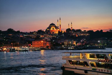 İstanbul, Türkiye 'de Eminonu İskelesi, Galata Köprüsü ve Süleyman Camii' nin muhteşem şehir ışıkları ve gün batımı manzarası İstanbul, Türkiye 'deki Bosporus yolcu teknelerinin bulunduğu pembe bir akşam gökyüzü altında.