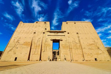 Edfu 'daki Horus Tapınağı' nın dış sütunlarının muhteşem manzarası MÖ 237 ile MÖ 57 yılları arasında Mısır 'ın Aswan yakınlarındaki parlak mavi gökyüzüne karşı Horus' un granit heykelleriyle inşa edilmiş.