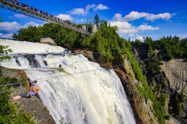 A thrill seeker on a zipline rushes across the thundering waters of the Montmorency Falls near Quebec city, the capital of Quebec province,Canada clipart