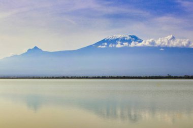 Afrika 'dan gelen kartpostal - Kenya' daki Amboseli Ulusal Parkı 'ndaki bu zamansız manzarada Amboseli Gölü' nün kar kaplı Kiyo zirvesi ve Mawenzie konisi gibi camlara yansıyan mükemmel bir resim