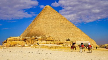 Turistler, Mısır 'ın Kahire yakınlarındaki Giza platosunda bulutlu gökyüzü olan Giza' da Büyük Khufu Piramidi yakınlarındaki çölde bir deve aldılar.