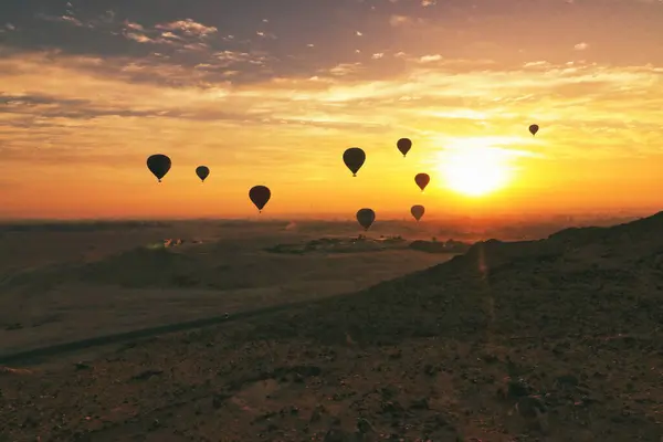 Sıcak hava balonlarının siluetleri sabahın erken saatlerindeki çöl güneşinin kızgın küresine karşı şafak vakti Mısır, Luxor 'da