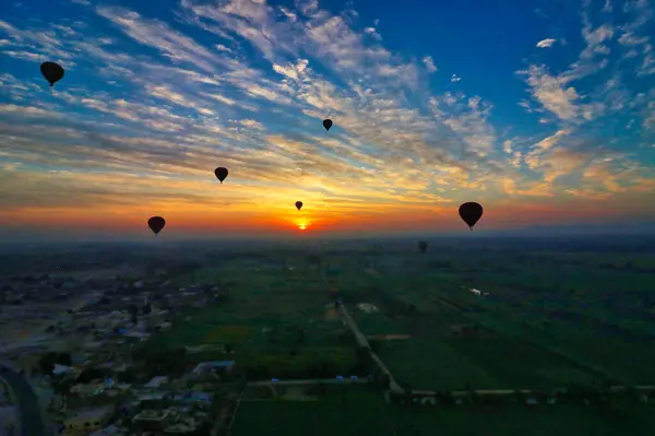 stock image A glowing sun rises over the fertile fields on the banks of the nile against a cloud streaked sky with silhouettes of Hot Air balloons operated by Luxor tour companies near Luxor,Egypt