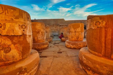 Luxor,Egypt,January 1,2020-A visitor enjoys a quite moment in the final hypostyle hall at the atmospheric Temple of Medinet Habu with Colonnade bases and reliefs built by the Pharoah Ramesess III clipart