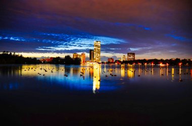 Magnificent azure tinged skies and evening cityscape views of the brightly lit skyline of the buildings along the beautiful Dows Lake in central Ottawa,Ontario,Canada clipart