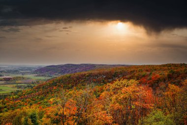 Champlain 'den öğleden sonraki bir sahnenin üzerinde kara yağmur bulutları süzülür. Gatineau Park, Quebec, Kanada' da canlı bir sonbahar renkleri yelpazesi vardır.