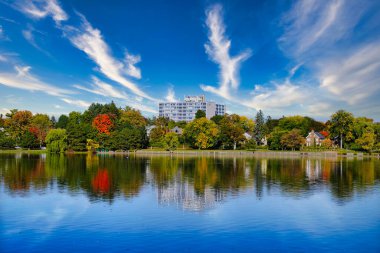 An Apartment building in the Glebe area amidst the changing colours of the Fall season with green,orange,red and yellow leaves on trees,wispy clouds in a blue sky in Autumn in Ottawa,Ontario,Canada clipart