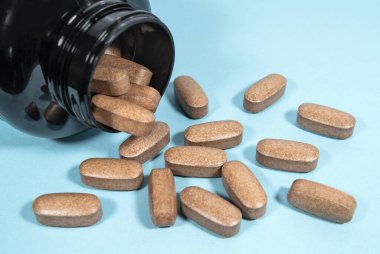 Kahverengi spor malzemeleri kapsülleri mavi arka planda siyah bir kavanozdan döküldü. Besleyici maddeler ve spor besinleri