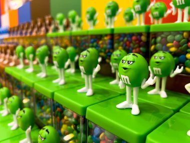 Londra, İngiltere - 6 Ağustos 2024: Ziyaretçiler ve tatlı meraklıları için renkli çikolata şekerlemelerinin yer aldığı M & M mağazasında sergilenen yeşil M & M şeker kutuları.