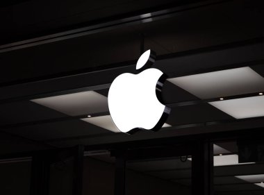 Basel, İsviçre - 23 Aralık 2024: Apple logosu koyu renkli bir Apple Store cephesinde parlıyor - Minimalist gece çekimi markanın modern estetiğini vurguluyor.
