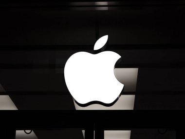 Basel, İsviçre - 23 Aralık 2024: Apple logosu koyu renkli bir Apple Store cephesinde parlıyor - Minimalist gece çekimi markanın modern estetiğini vurguluyor.