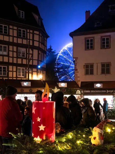 Colmar, Fransa - 26 Aralık 2024: Colmar Noel Pazarı 'nda parlayan yıldız kesimleriyle süslü mum dekorasyonu, arka planda mavi ışıkta parlayan dönme dolap..