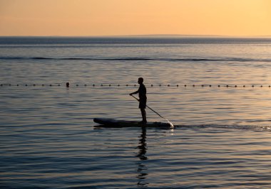 Gün batımında sakin denizde kürek çeken bir insanın silueti..