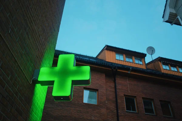 green neon cross, pharmacy hospital sign on a building, evening blue light