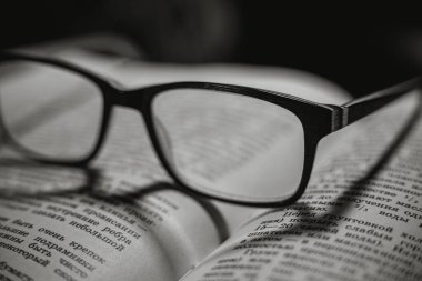 Sayfaları ve okuma gözlüğü olan eski bir kitap, siyah arka plan. Kitaptaki gölgeler bir kalbin şeklini temsil ediyor.. 
